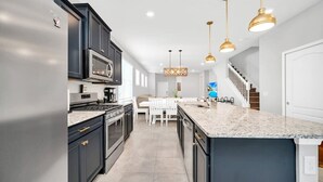 A modern kitchen with dark cabinetry, a large island, and pendant lighting. - Private Pool | Gated Resort | 15 Min to Disney 7299 (Davenport)