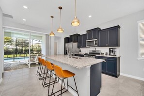 A modern kitchen with dark cabinets, a large island with bar stools, and a view of a swimming pool.