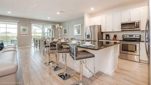 A modern kitchen with white cabinets, stainless steel appliances, and a bar area with stools.