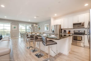 Una cocina moderna con armarios blancos, electrodomésticos de acero inoxidable y una zona de bar con taburetes.