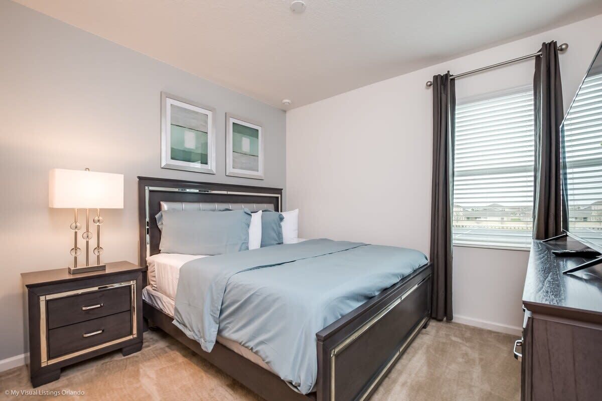 A bedroom with a bed, bedside table, lamp, and a window with curtains.