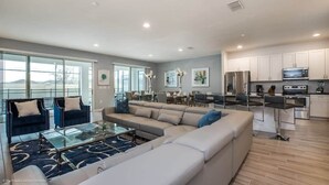 A modern living room with a sectional sofa, a glass coffee table, and a dining area with a kitchen in the background.