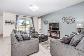 Una sala de estar moderna con sofás grises, un sillón estampado, un televisor sobre un mueble de madera y decoración en la pared.