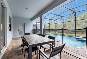 A covered patio with a pool, a dining table, and chairs.