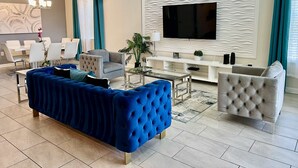 Ein stilvolles Wohnzimmer mit einem blauen Sofa, einem grauen Sessel, einem Glastisch, einer weißen Unterhaltungseinheit und einem flachbildfernseher an der Wand.