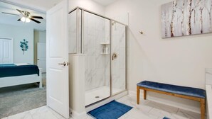 A bathroom with a glass shower enclosure, a bench, a blue rug, and a painting on the wall. - Game Room | No Rear Neighbors | 4 Miles Disney 2709 (Kissimmee)