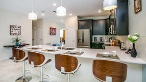 A modern kitchen with a central island, bar stools, and pendant lighting. - Game Room | No Rear Neighbors | 4 Miles Disney 2709 (Kissimmee)