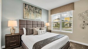 A bedroom with a large bed, two bedside tables, a window with blinds, and a wall-mounted abstract art piece. - Splash Pool | Air Hockey | Lazy River | Disney 2755 (Kissimmee)