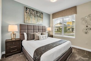A bedroom with a large bed, two bedside tables, a window with blinds, and a wall-mounted abstract art piece.
