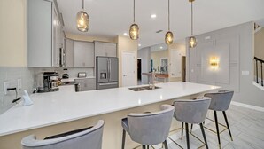 Una cocina moderna con una isla grande, taburetes de bar e iluminación colgante.