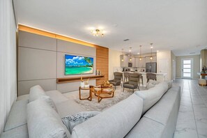 Una sala de estar moderna con un sofá grande, una mesa de centro y un televisor montado en la pared.
