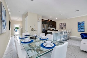A modern dining area with a glass table, white chairs, and blue placemats. - Disney Theme | Pool | Lazy River | Disney 2861 (Kissimmee)