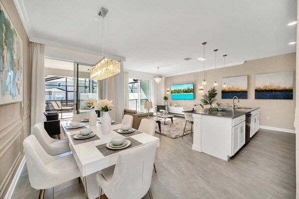 Une cuisine moderne avec des meubles blancs, un îlot central et un coin repas comprenant une table et des chaises blanches.