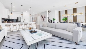 Ein modernes Wohnzimmer mit einem weißen Sofa, einem Couchtisch und einer Küche im Hintergrund.