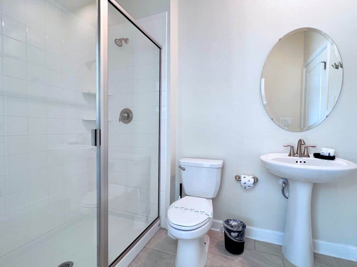 Une salle de bain avec une douche à parois de verre, des toilettes et un lavabo sur colonne avec un miroir au-dessus.