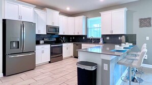 A modern kitchen with white cabinets, stainless steel appliances, and a central island with bar stools. - Star Wars | Avengers | Pool | Resort | Disney 4544 (Kissimmee)