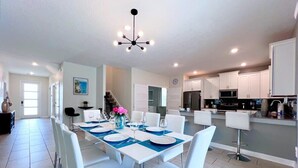 A modern kitchen with white cabinets, a central island, and a dining area with white chairs and a blue tablecloth. - Star Wars | Avengers | Pool | Resort | Disney 4544 (Kissimmee)