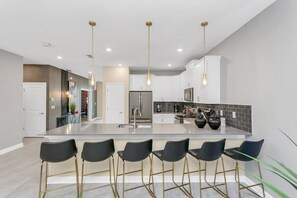 Une cuisine moderne dotée d’un îlot central, de tabourets de bar et de luminaires suspendus.