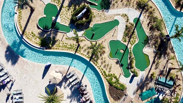 Vista aérea de un complejo turístico con múltiples piscinas, tumbonas y palmeras.