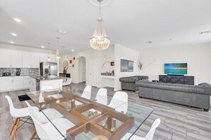 A modern kitchen with white cabinets, a stainless steel refrigerator, and a glass dining table with white chairs.