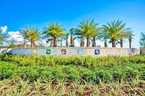 Stroll through a serene landscaped area surrounded by palm trees and a low wall featuring symbols of wellness and accessibility.