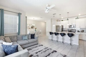 A modern kitchen with white cabinets, a central island with bar stools, a dining area with a table and chairs, and a living room with a sofa and a coffee table. - Star Wars & Coastal! Resort 6 mi 2 Disney! 4832 (Kissimmee)