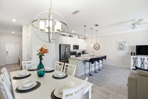A modern kitchen with a central island, white dining chairs, a table set for four, and a pendant light above. - Star Wars & Coastal! Resort 6 mi 2 Disney! 4832 (Kissimmee)