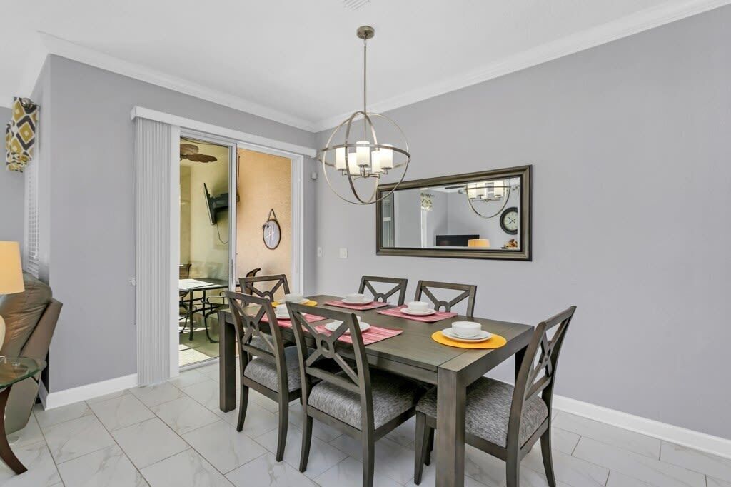 Un coin repas avec une table dressée pour quatre personnes, un lustre et un miroir au mur.