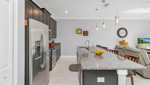 Una cocina moderna con una isla central, electrodomésticos de acero inoxidable y una zona de comedor con sofá y televisor.