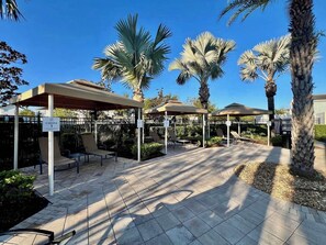 Un espace extérieur aménagé, abrité et doté de palmiers, avec un chemin pavé et un panneau indiquant « CABANE 1 ».