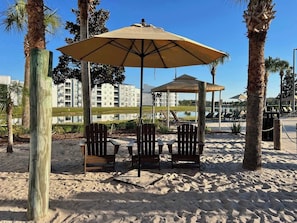 A beach area with wooden chairs, a large umbrella, and a gazebo.