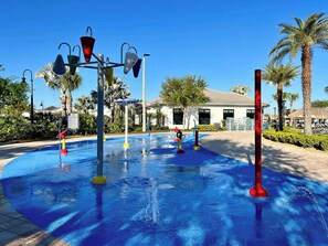 A water play area with various structures, palm trees, and a building in the background.