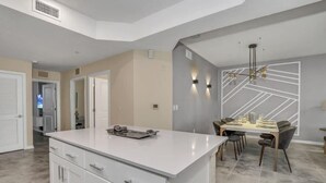 A modern kitchen with a central island, a dining area with a table and chairs, and a unique geometric wall design. - Great Value | Lazy River | 4 Miles to Disney 3180 (Kissimmee)