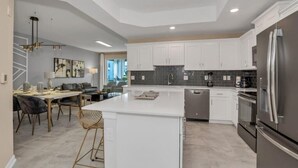 A modern kitchen with white cabinets, a central island, stainless steel appliances, and a dining area with a table and chairs. - Great Value | Lazy River | 4 Miles to Disney 3180 (Kissimmee)