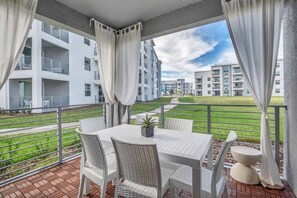 Un balcon avec une table et des chaises, donnant sur un espace verdoyant et des immeubles.