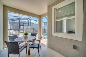 A covered patio with a round table and chairs, a potted plant, and a view of a swimming pool and buildings in the background. - Value! Clean! Lazy River-Resort 6 mi 2 Disney-4228 (Kissimmee)