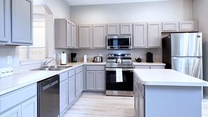 A modern kitchen with grey cabinets, stainless steel appliances, and a white countertop.