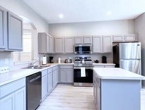 A modern kitchen with grey cabinets, stainless steel appliances, and a white countertop.