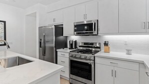 A modern kitchen with stainless steel appliances, white cabinetry, and a marble countertop. - Desert Serenity | Pool, Spa, BBQ, Near Courses (La Quinta)