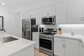 A modern kitchen with stainless steel appliances, white cabinetry, and a marble countertop. - Desert Serenity | Pool, Spa, BBQ, Near Courses (La Quinta)