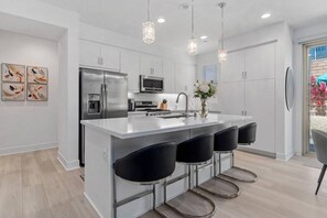A modern kitchen with a central island, bar stools, stainless steel appliances, and pendant lighting.