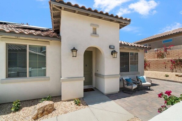 A residential building with a tiled roof, a covered patio with outdoor furniture, and a small archway entrance.
