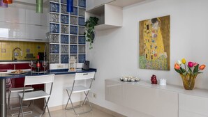 A modern kitchen with a glass block backsplash, white cabinets, and a dining area with two chairs. - Siena: appartamento panoramico con terrazza, wi-fi e aria condizionata (Siena)