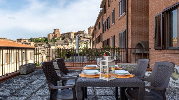 A rooftop terrace with a table set for four, surrounded by chairs, overlooking a historic cityscape. - Siena: appartamento panoramico con terrazza, wi-fi e aria condizionata (Siena)