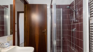 A bathroom with a wooden door, a white sink, and a glass shower enclosure. - Siena: appartamento panoramico con terrazza, wi-fi e aria condizionata (Siena)