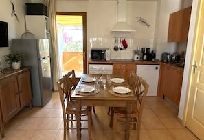 Una cocina con una mesa de comedor preparada para cuatro personas, un refrigerador, microondas y varios electrodomésticos.