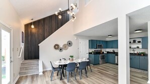 Une cuisine moderne avec des meubles bleus, un coin repas avec une table ronde et des chaises, et un escalier avec une finition en bois foncé.