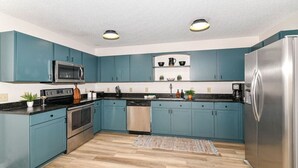 Une cuisine moderne avec des meubles de couleur turquoise, des appareils en acier inoxydable et un plancher en bois.