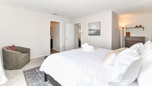 Une chambre à coucher avec un lit, une chaise, un tapis, un tableau et une table de chevet avec une lampe.