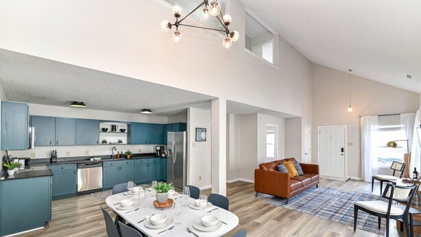 Une cuisine moderne avec des meubles de couleur turquoise, un coin repas avec une table blanche et un salon avec un canapé marron.